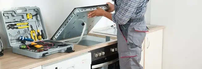 Cooktop repair technician lifting a built-in stovetop for service in Rockford, IL