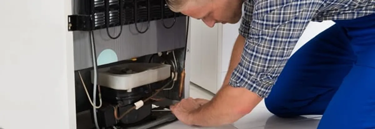 Refrigerator repair technician servicing the compressor and condenser area in Rockford, IL