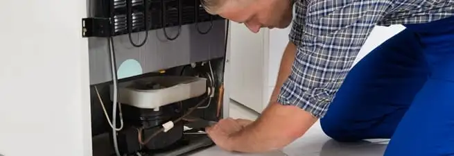 Refrigerator repair technician servicing the compressor and condenser area in Rockford, IL