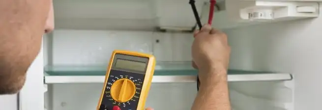 Refrigerator repair technician testing electrical components with a multimeter in Rockford, IL